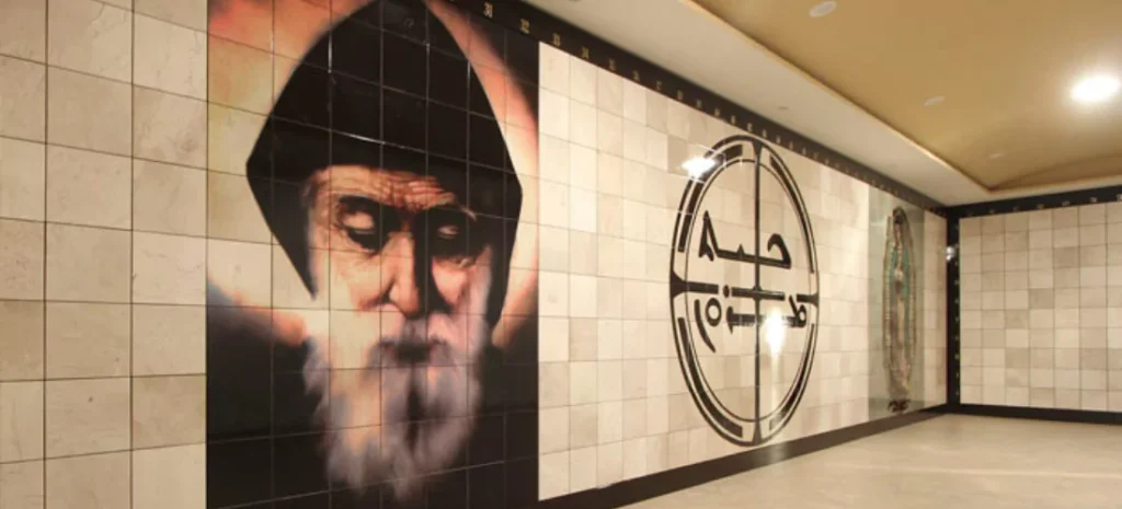 Muro de nichos decorado con la imagen de San Charbel, un símbolo central religioso y la Virgen de Guadalupe al fondo, creando un espacio de devoción y recogimiento.